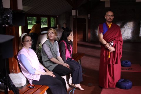 Aktorzy na planie serialu "Siła wyższa" w Folwarku Badowo. Mnich i kobiety siedzące na ławce.