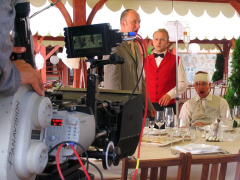 Aktorzy na planie filmu Testosteron w Folwarku Badowo. Widok zza kamery, scena przy stole.