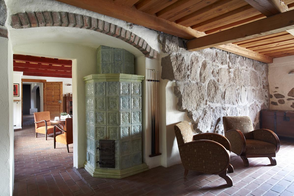 Sala bilardowa wejście, obok wejścia kominek, kije bilardowe na ścianie po prawej dwa fotele na tle kamiennej ściany